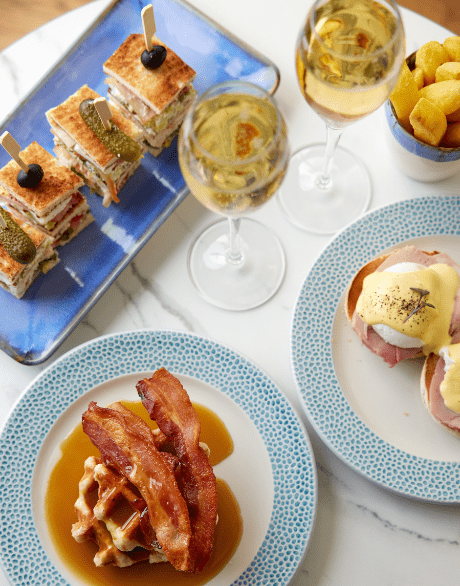 Brunch spread with champagne, club sandwiches, eggs Benedict, and waffle with bacon