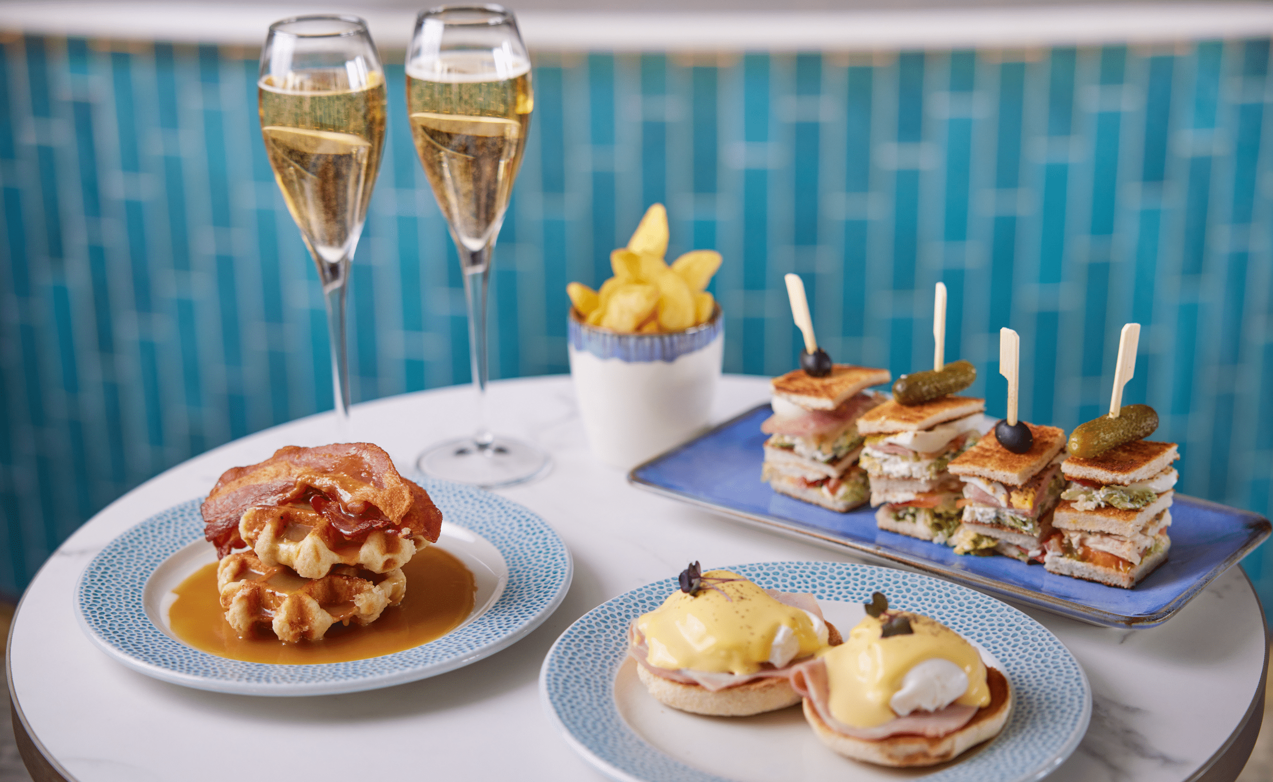 Brunch spread with champagne, club sandwiches, eggs Benedict, and waffle with bacon