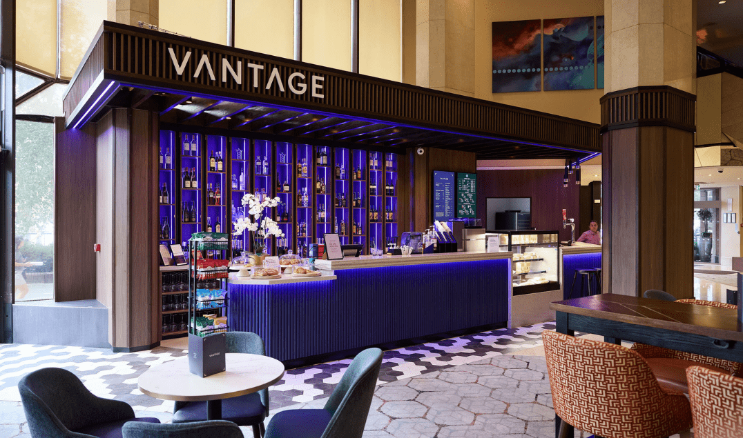 Vantage at The Tower Hotel, featuring illuminated shelving, a contemporary service counter, and lounge seating.