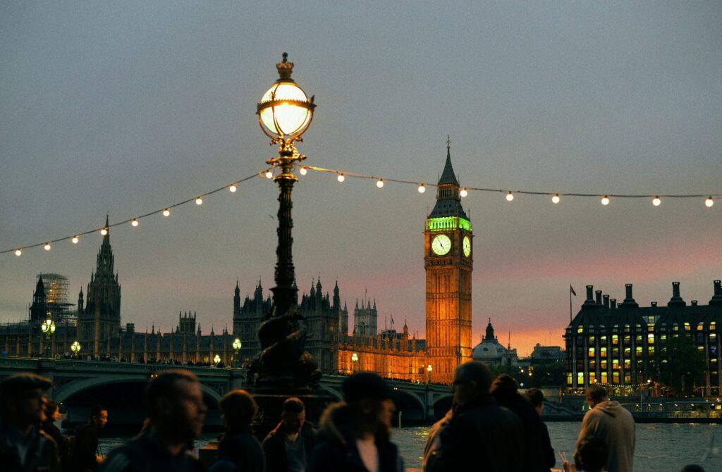 Big Ben and the Houses of Parliament illuminated at dusk, with people and string lights along the South Bank.