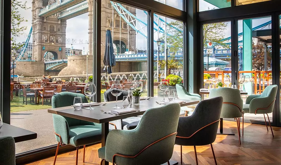 A table and chairs in the Vicinity restaurant at the Tower Hotel situated in front of a large window with The Tower of London in the background