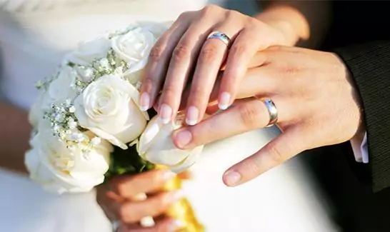 Married couples hands with their new rings and bride holding white flowers