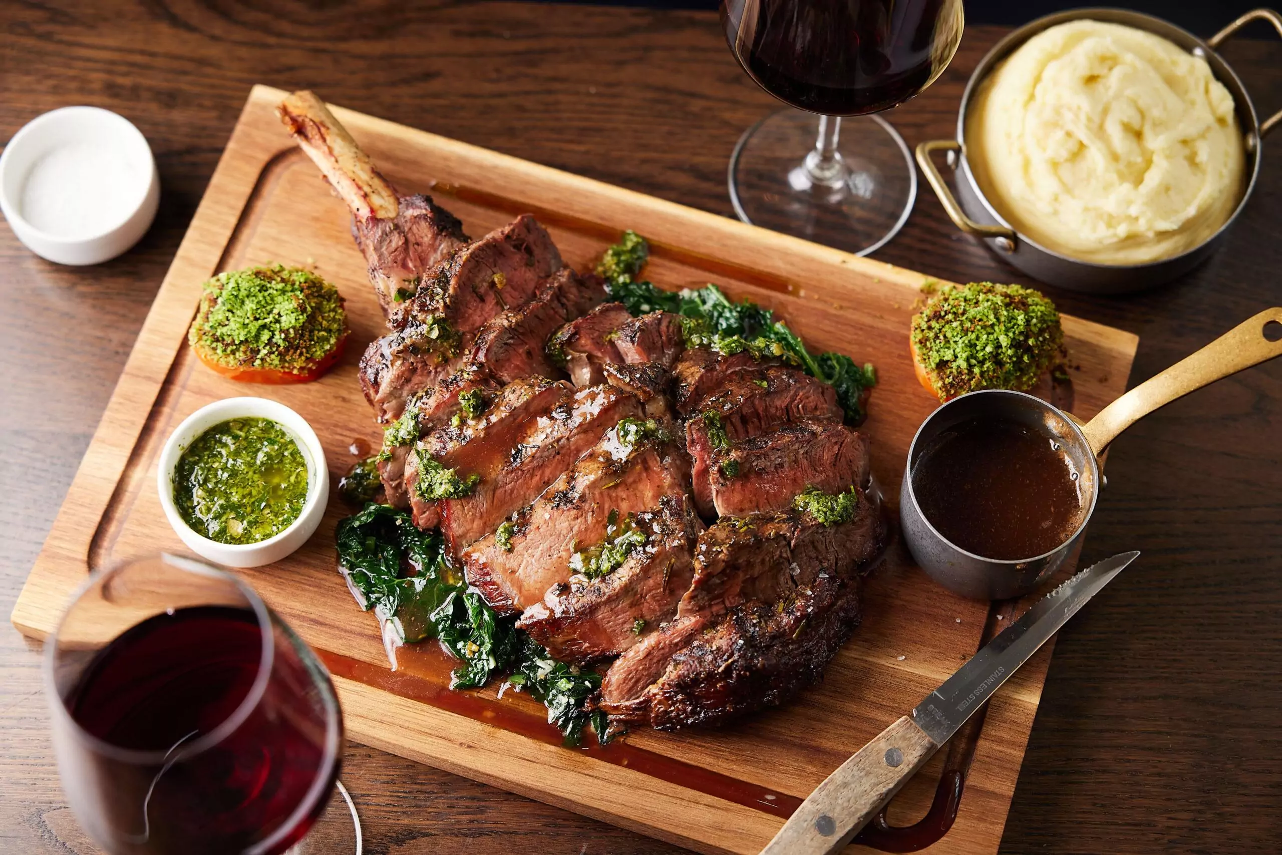 Tomahawk steak sliced on a wooden board, with mash and gravy