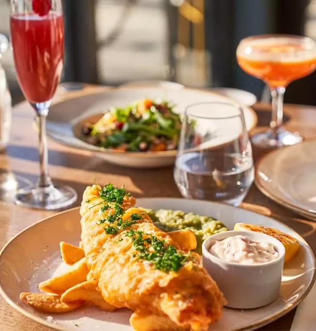 Fish and chips dish with cocktails in the background