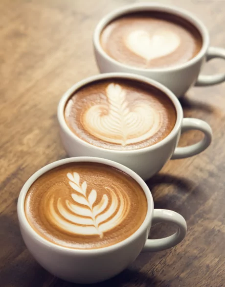 Three cups of latte with heart, tulip, and leaf art on a wooden table