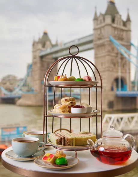 Afternoon tea stand with pastries, scones, and sandwiches, set against Tower Bridge
